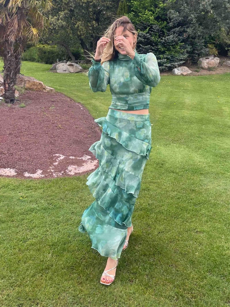 Conjunto Emerald de Baymo verde, blusa de manga larga y falda de volantes en diagonal, en un jardín
