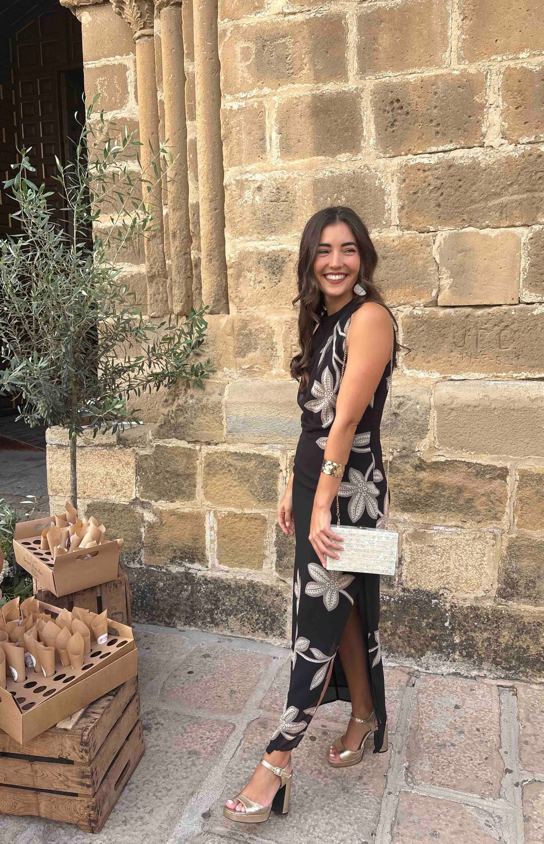Vestido midi negro sin mangas con flores blancas y abertura lateral de Lady Pipa, junto a un muro de piedra
