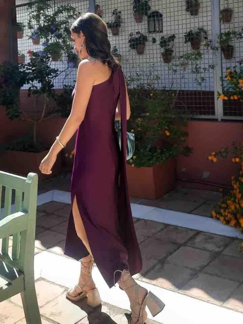 Vestido midi ciruela de The Are, de un hombro con lazada larga en la espalda y abertura, con sandalias nude, en una boda de día en octubre