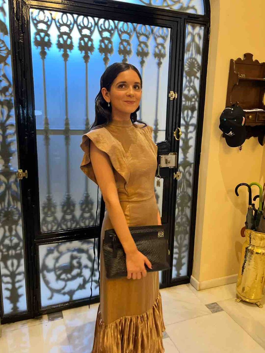 Vestido bronce de The IQ Collection ante una cancela de hierro, con cartera negra